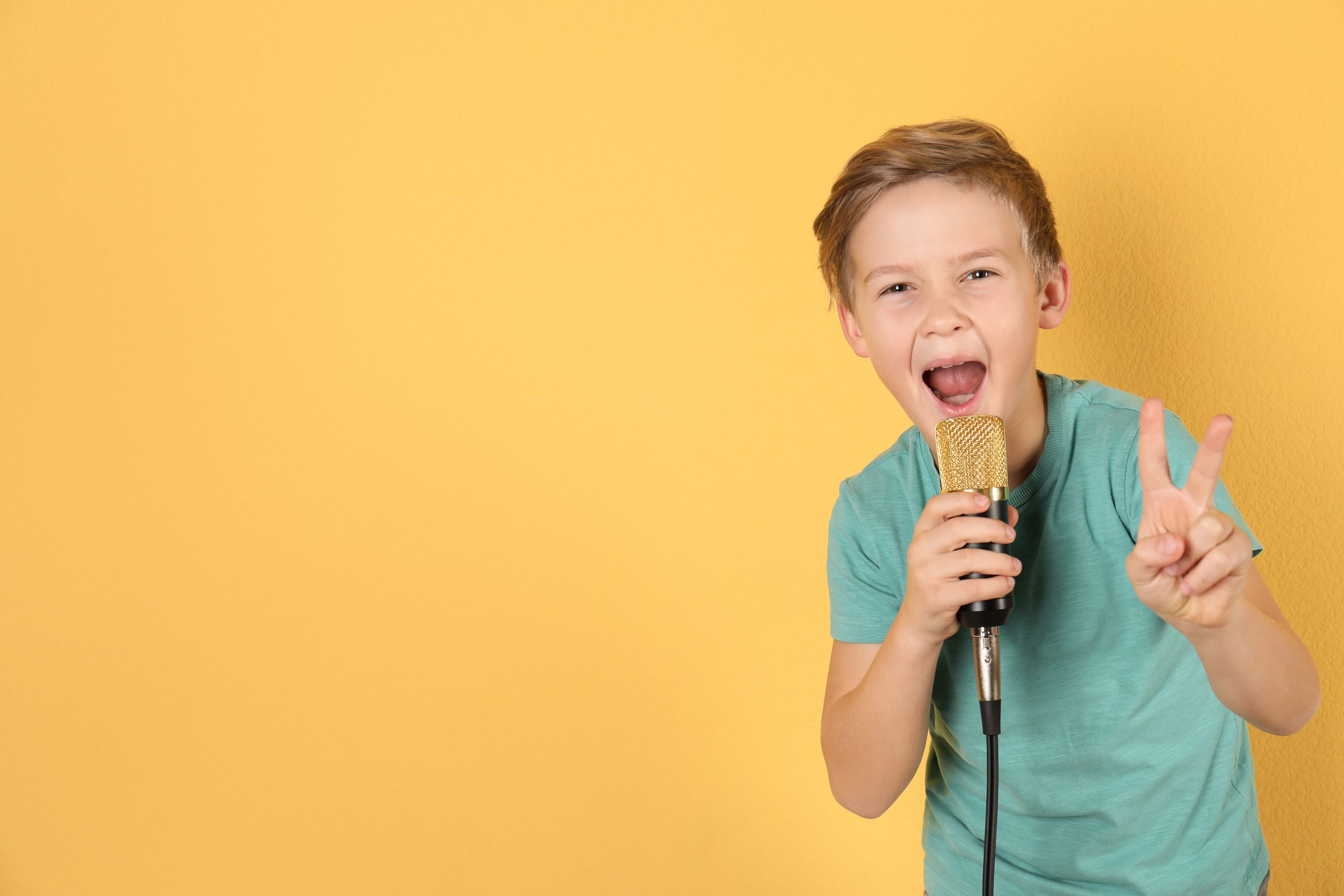 Cute boy singing in microphone on color background. Space for text